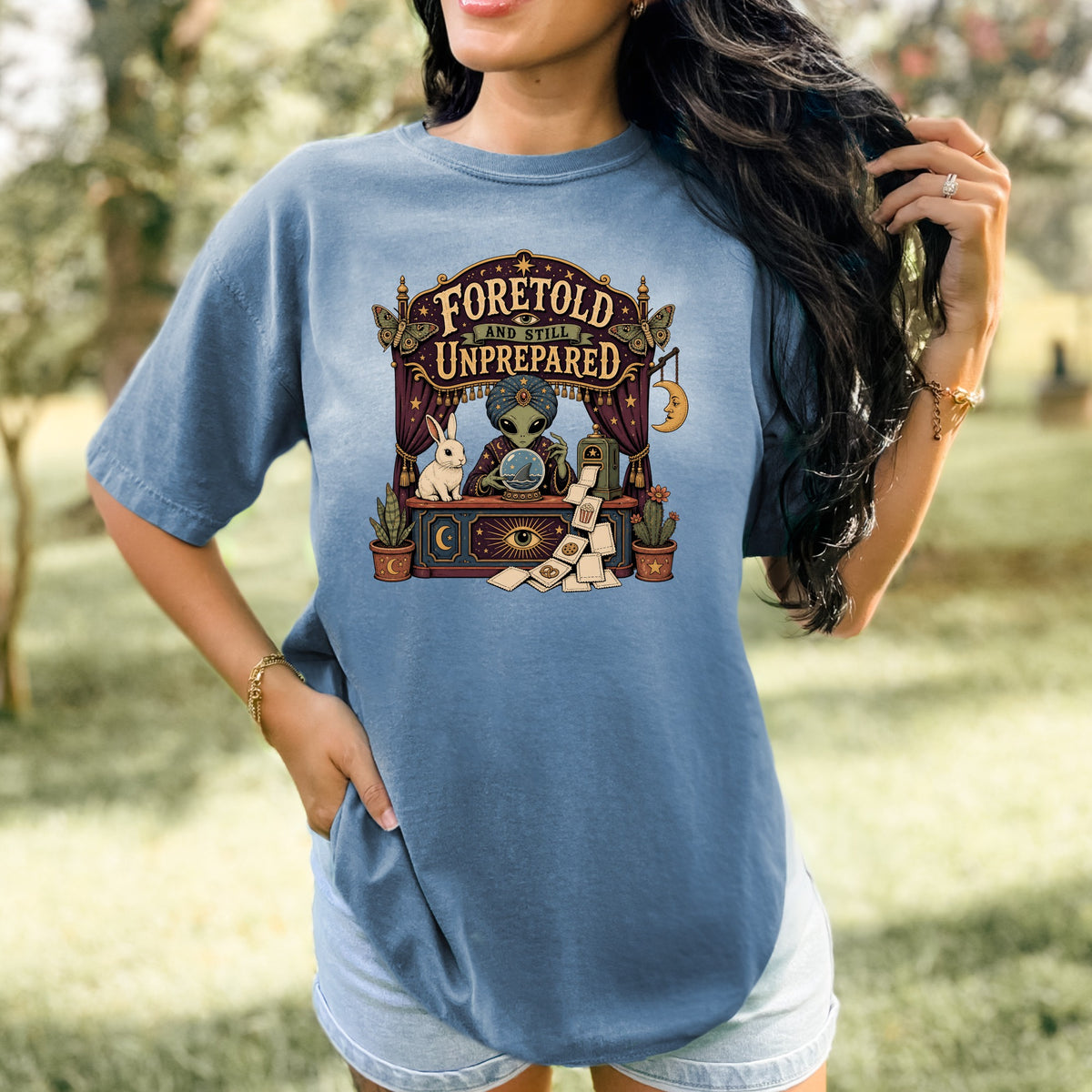 T-shirt graphic: Alien fortune teller with rabbit, crystal ball, and text "Foretold and Still Unprepared".