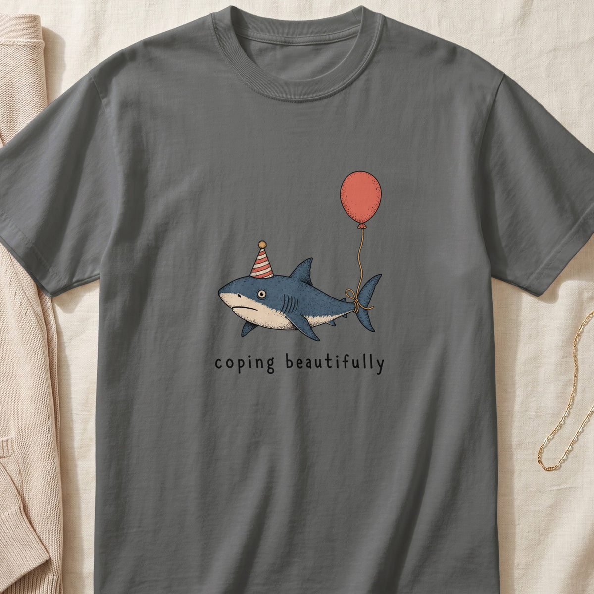 Shark wearing party hat holding balloon with text "coping beautifully."