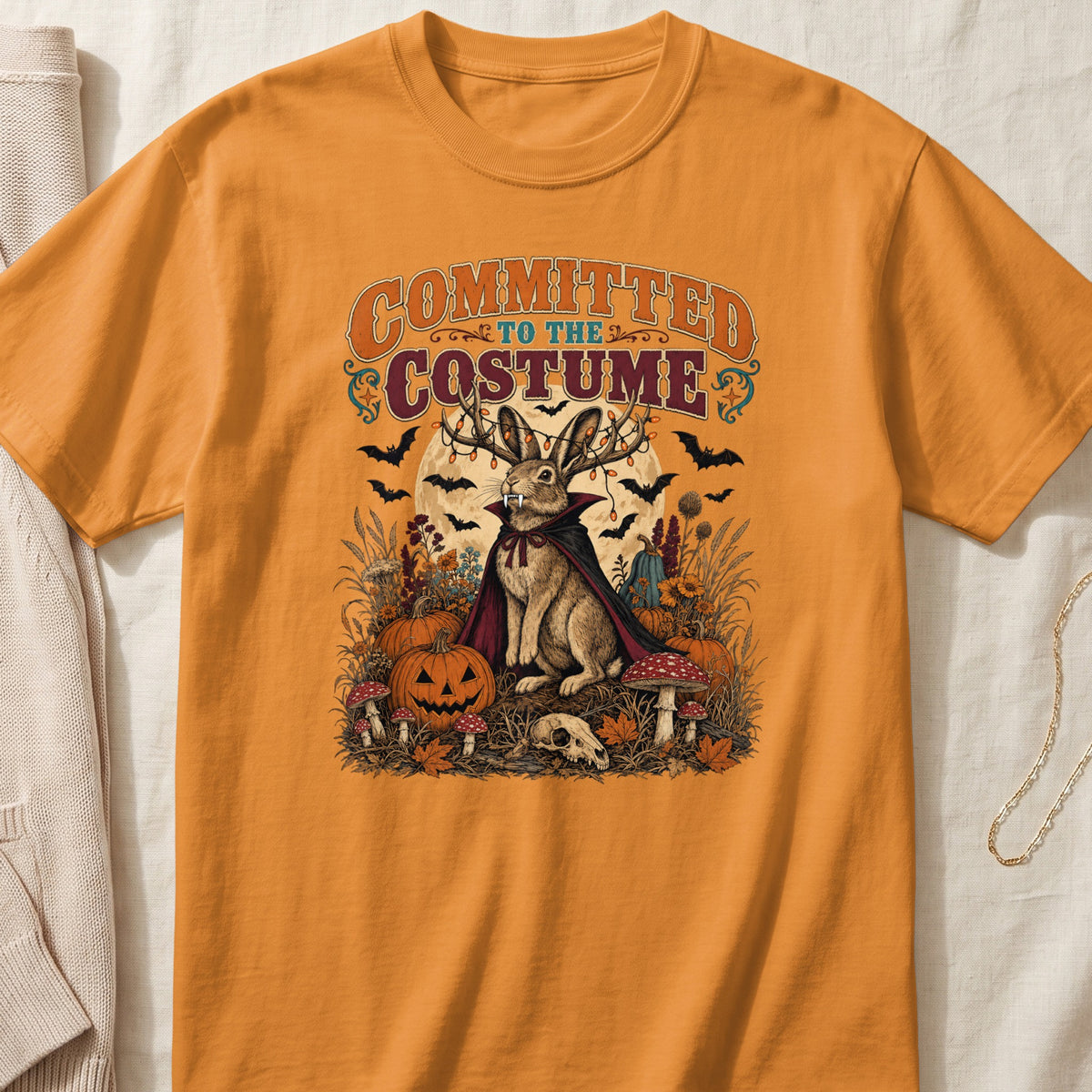 Orange t-shirt graphic with bunny in vampire costume, bats, pumpkins, and text "Committed to the Costume".