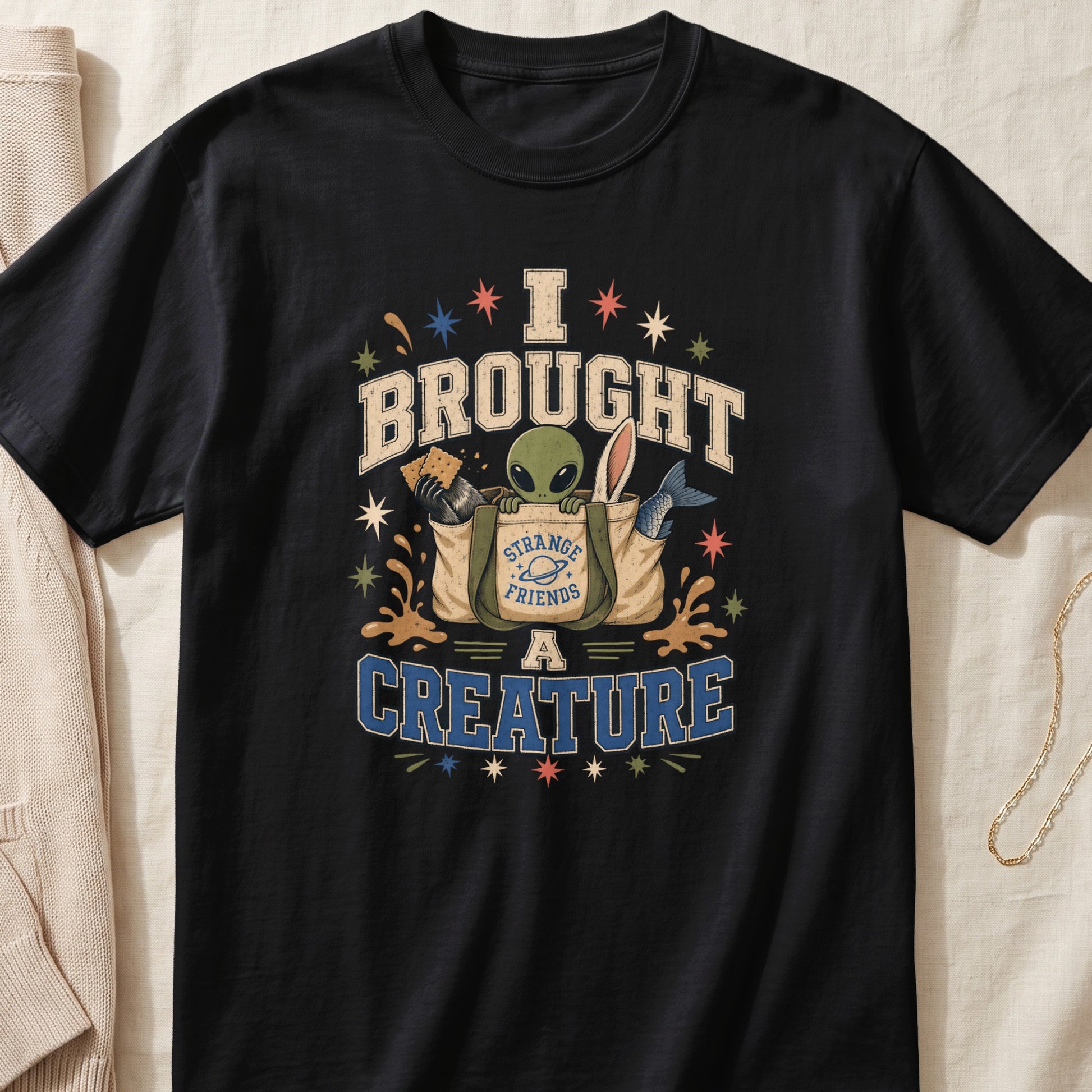 Black t-shirt with "I BROUGHT A CREATURE" graphic featuring an alien in a bag.