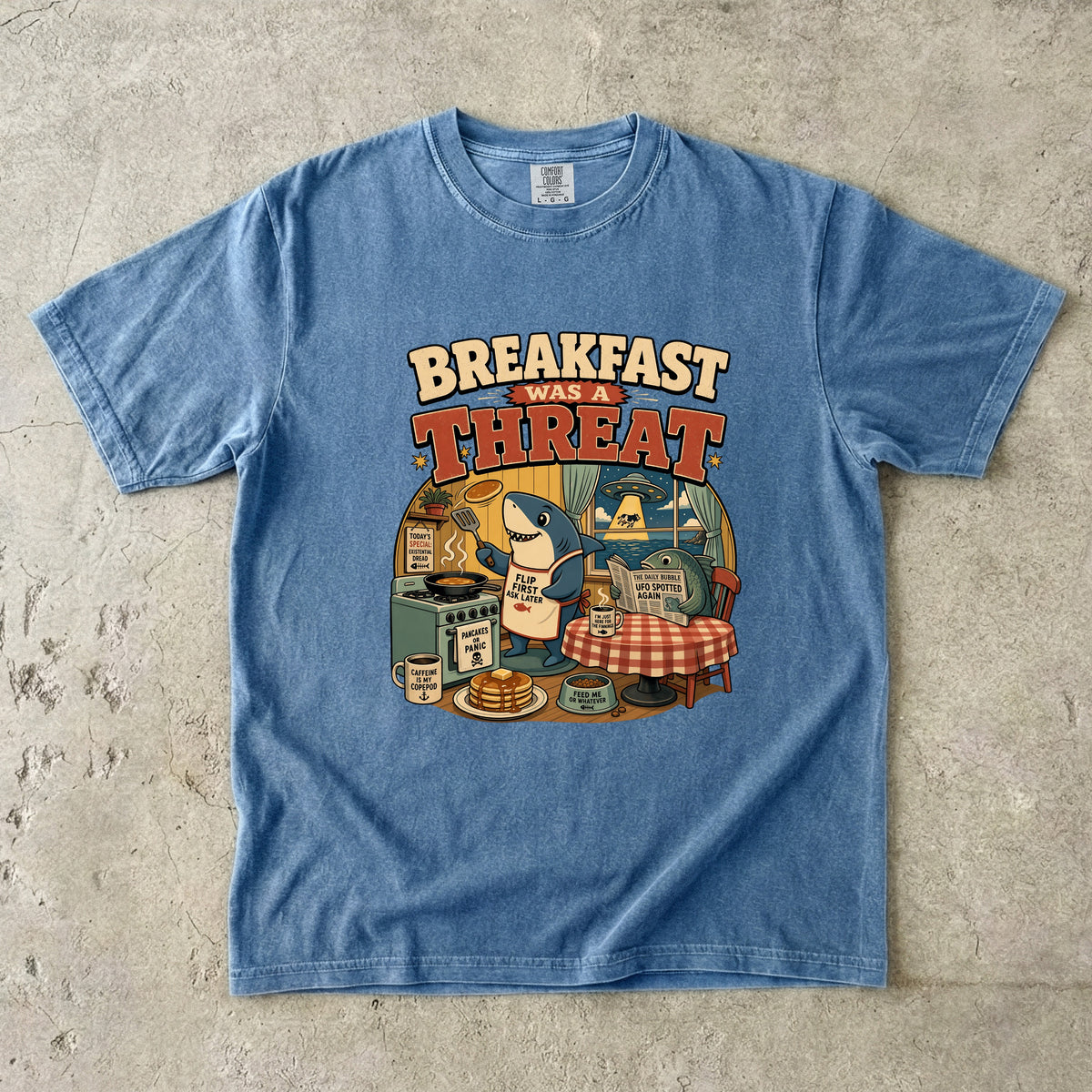 Blue t-shirt with graphic "Breakfast Was a Threat" featuring a shark making pancakes.