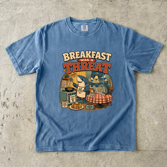 Blue t-shirt with graphic "Breakfast Was a Threat" featuring a shark making pancakes.