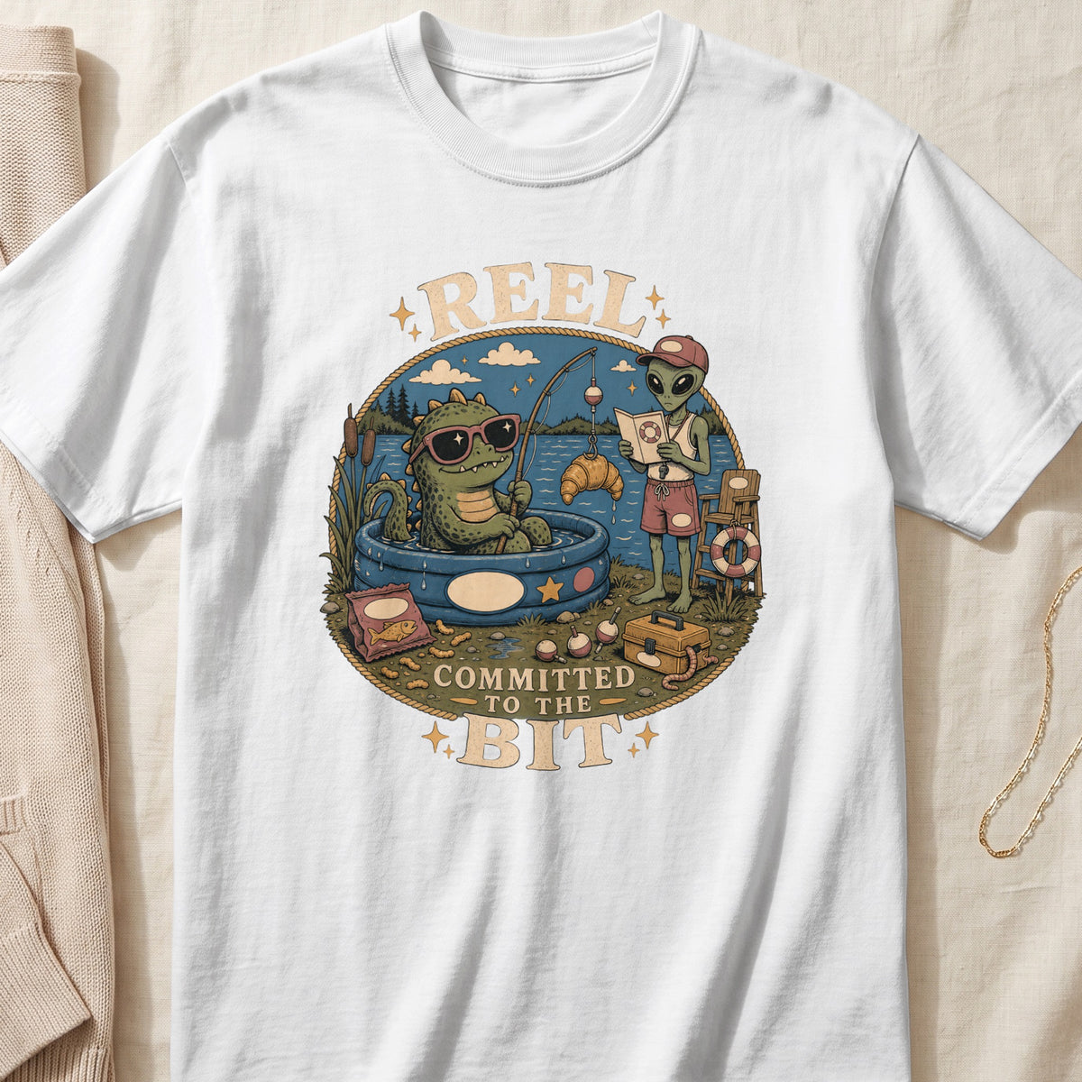 Graphic t-shirt with a cartoon of a dinosaur and an alien fishing, text reads "REEL COMMITTED TO THE BIT".
