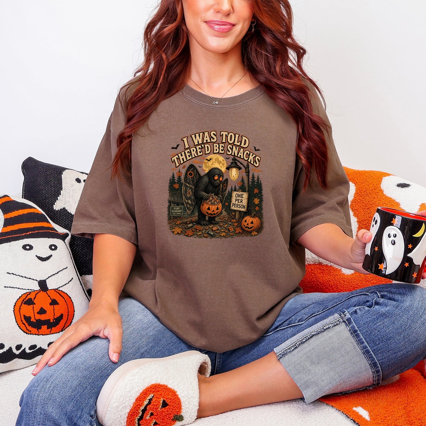 Brown t-shirt with a graphic featuring a Mothman-like creature and text "I WAS TOLD THERE'D BE SNACKS."