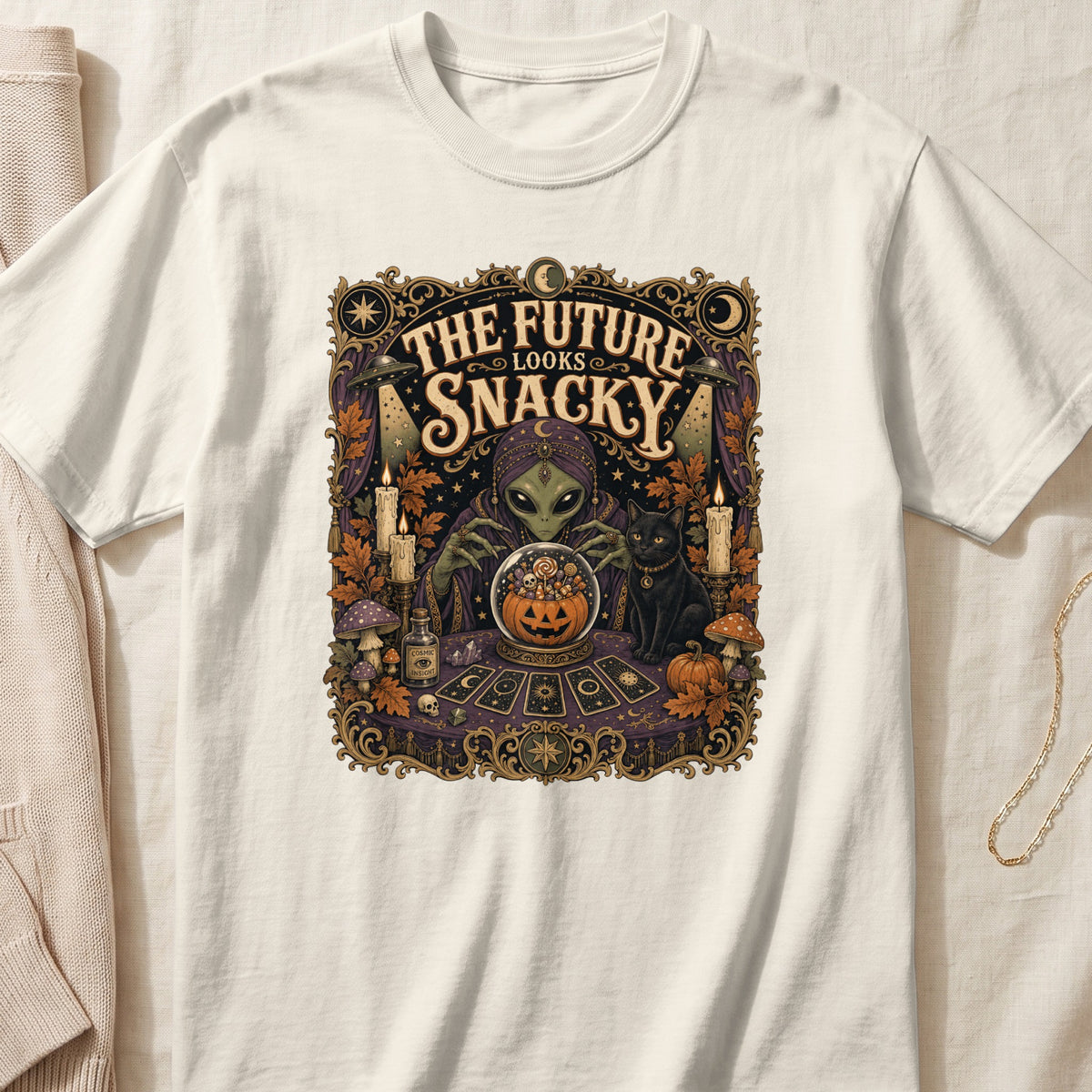 Alien fortune teller with a black cat and candy-filled crystal ball, reads "The Future Looks Snacky".