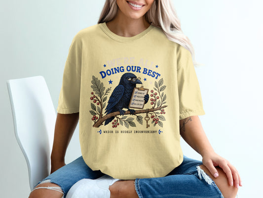 Light yellow t-shirt with raven, clipboard, and text: "We're all doing our best."