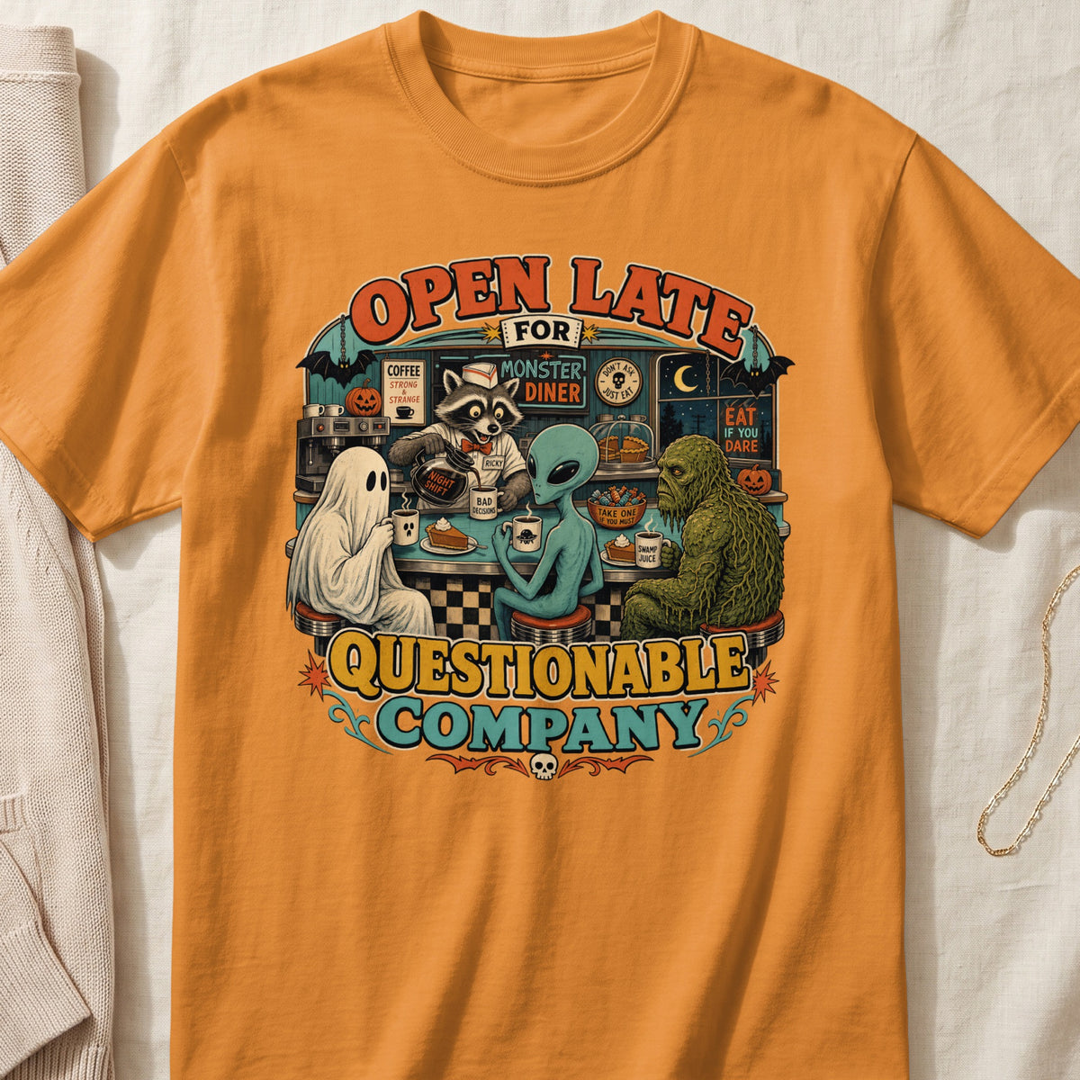 Orange t-shirt with graphic: Open Late for Monster Diner, featuring a ghost, alien, raccoon, and swamp monster.