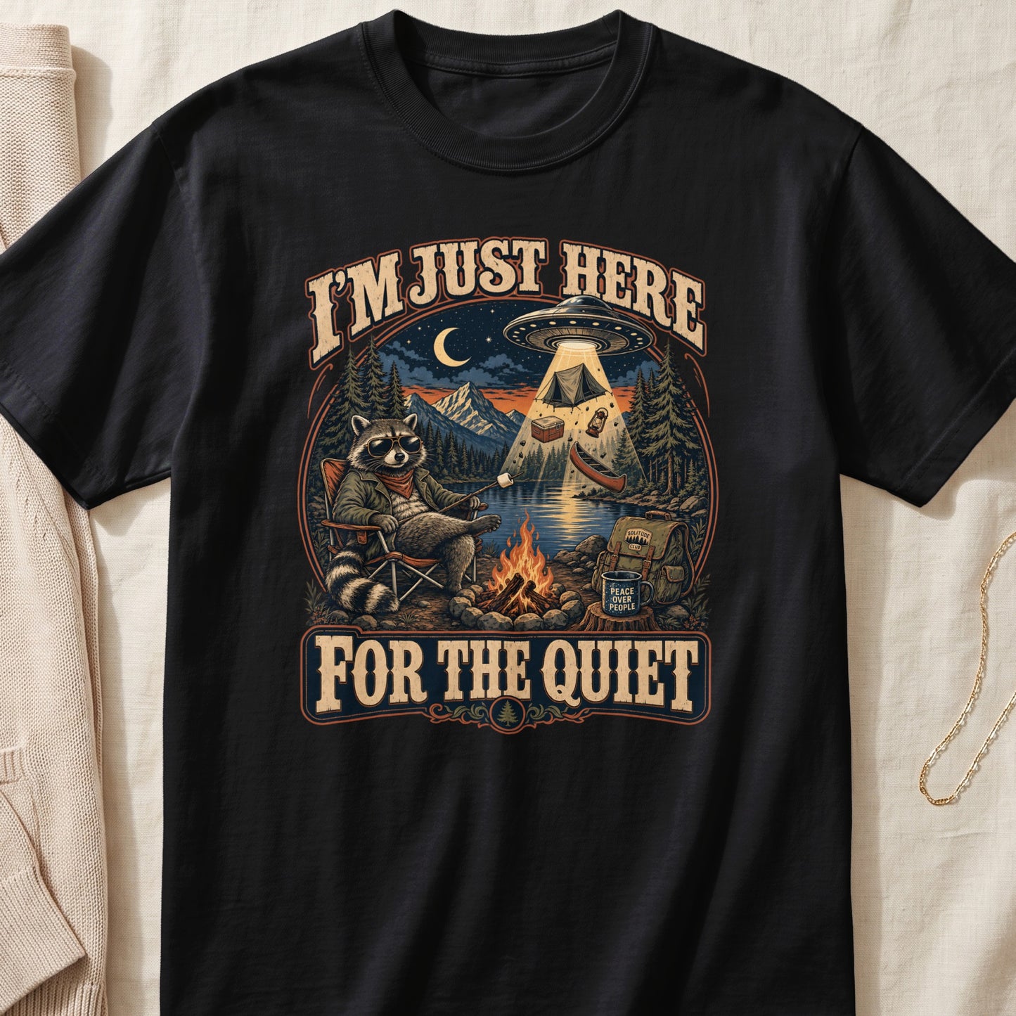 Black t-shirt with vintage graphic of raccoon camping under a UFO and text "I'M JUST HERE FOR THE QUIET".