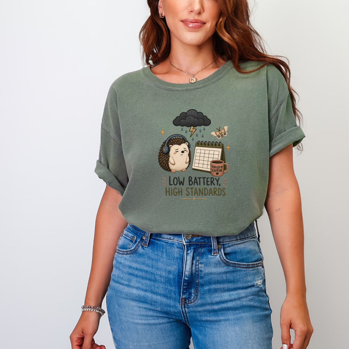 Green t-shirt with a hedgehog wearing headphones, under a rain cloud, with text "LOW BATTERY, HIGH STANDARDS".