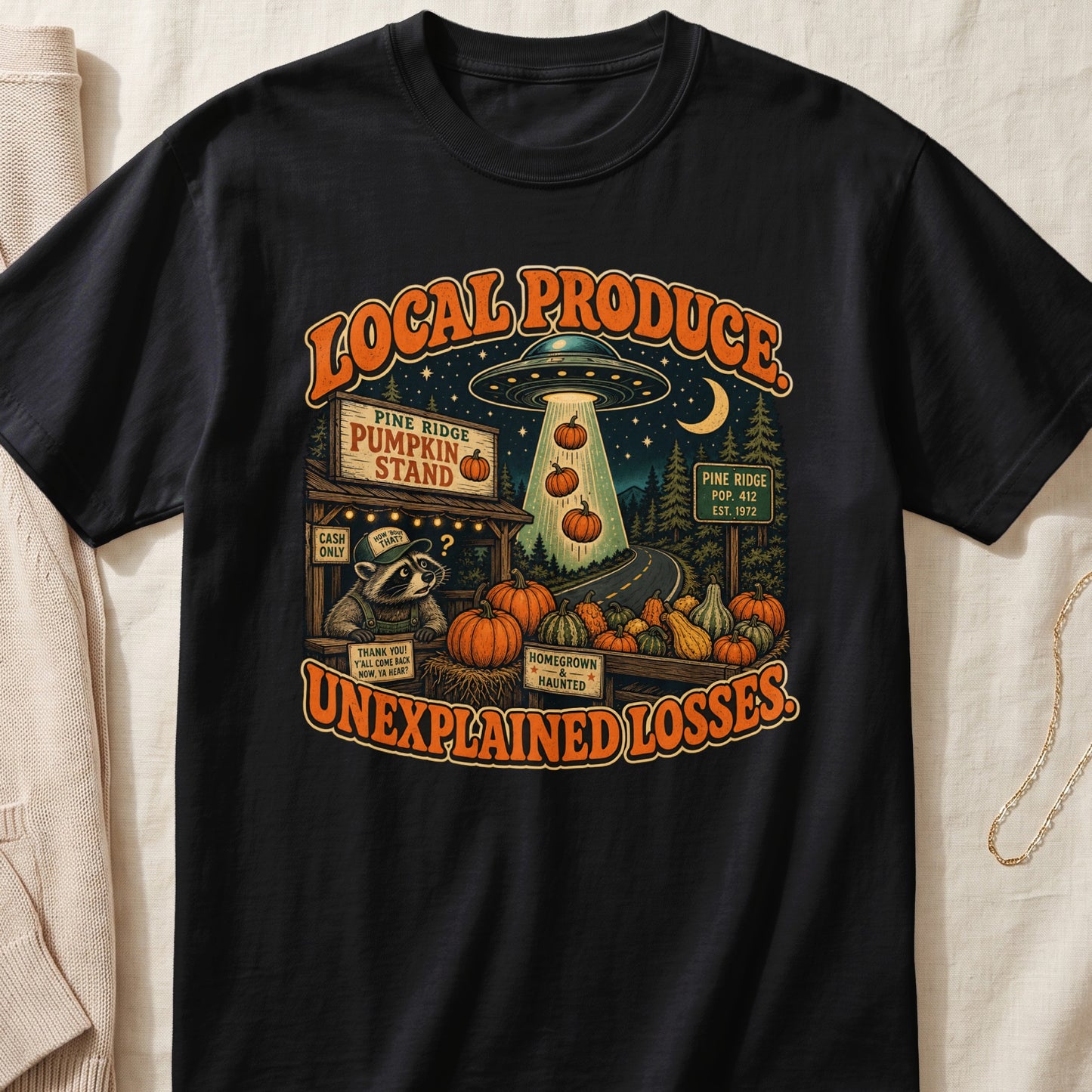 Black t-shirt with "Local Produce Unexplained Losses" text, alien, raccoon, and pumpkins.