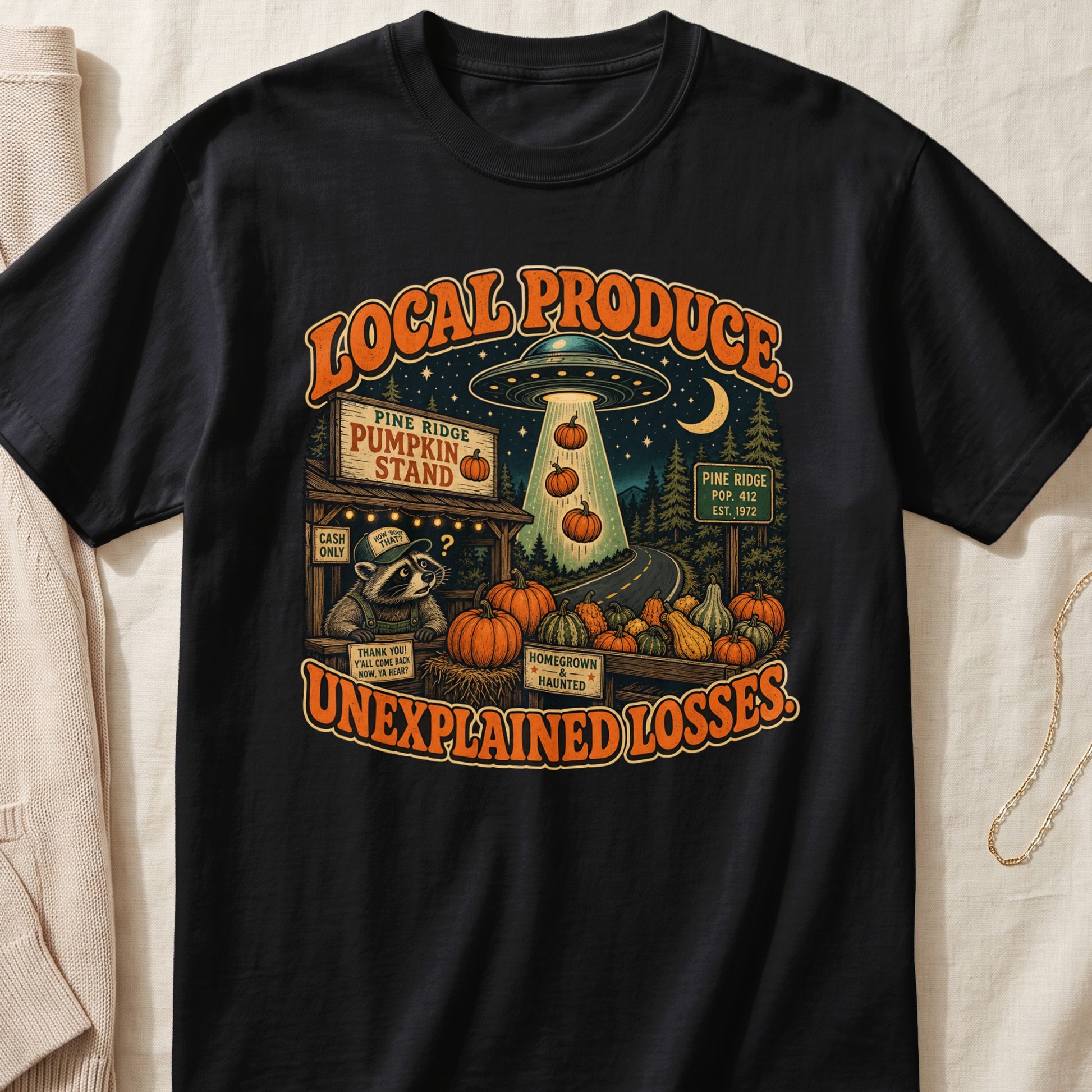 Black t-shirt with "Local Produce Unexplained Losses" text, alien, raccoon, and pumpkins.