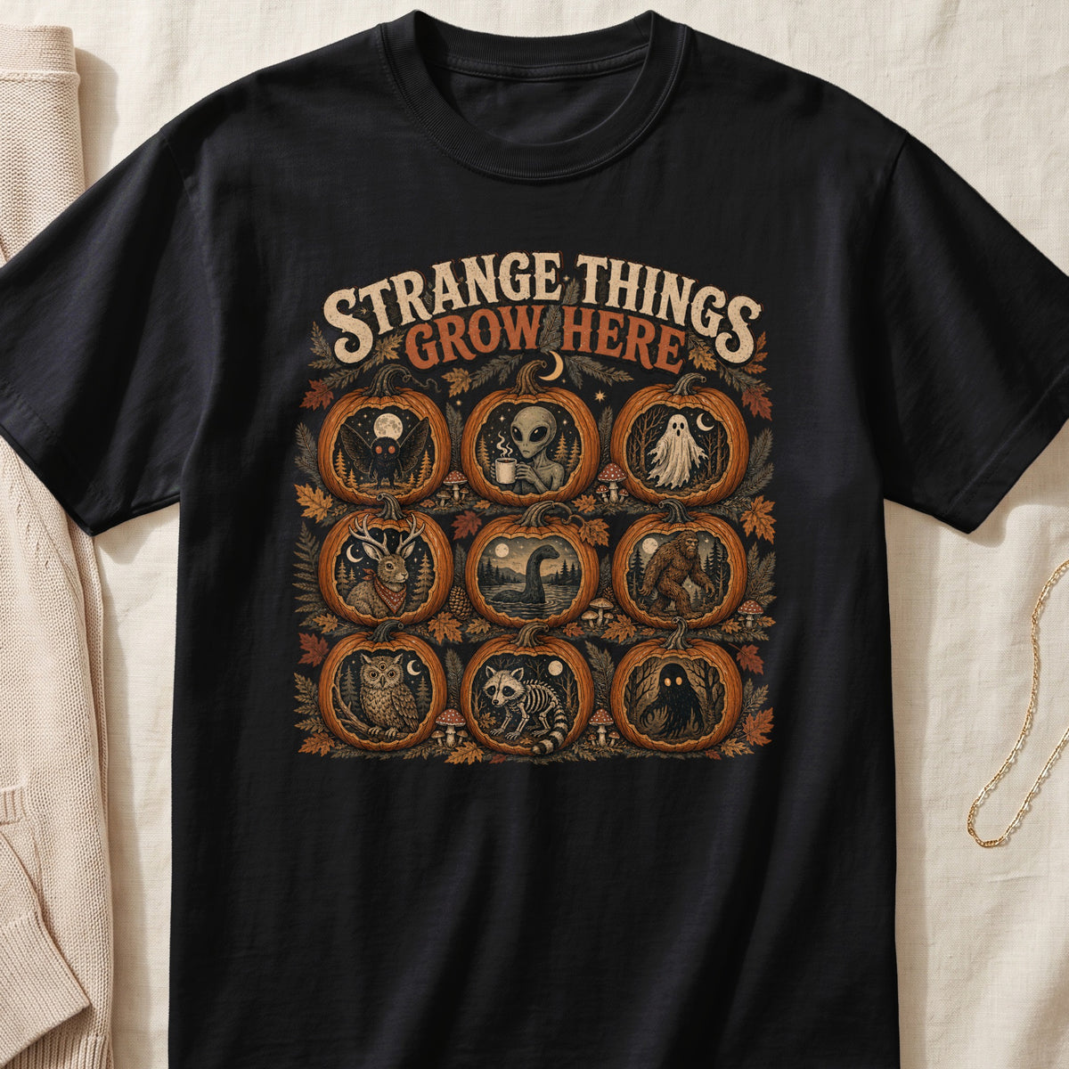 Black t-shirt with pumpkins featuring mothman, alien, ghost, deer, loch ness, bigfoot, owl, raccoon, and a cloaked figure.
