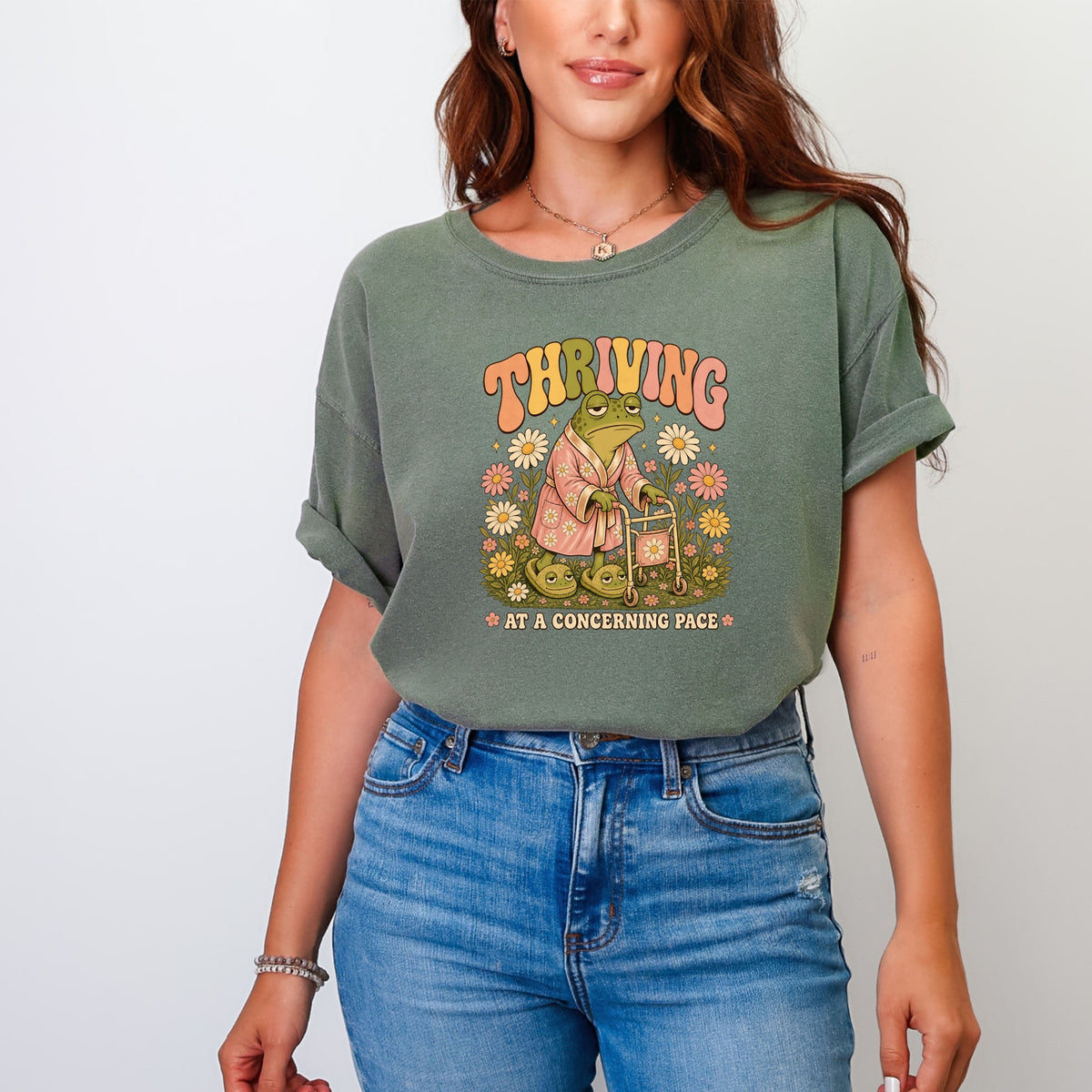 Retro graphic of a frog in a robe with a walker and flowers, text "THRVING AT A CONCERNING PACE".