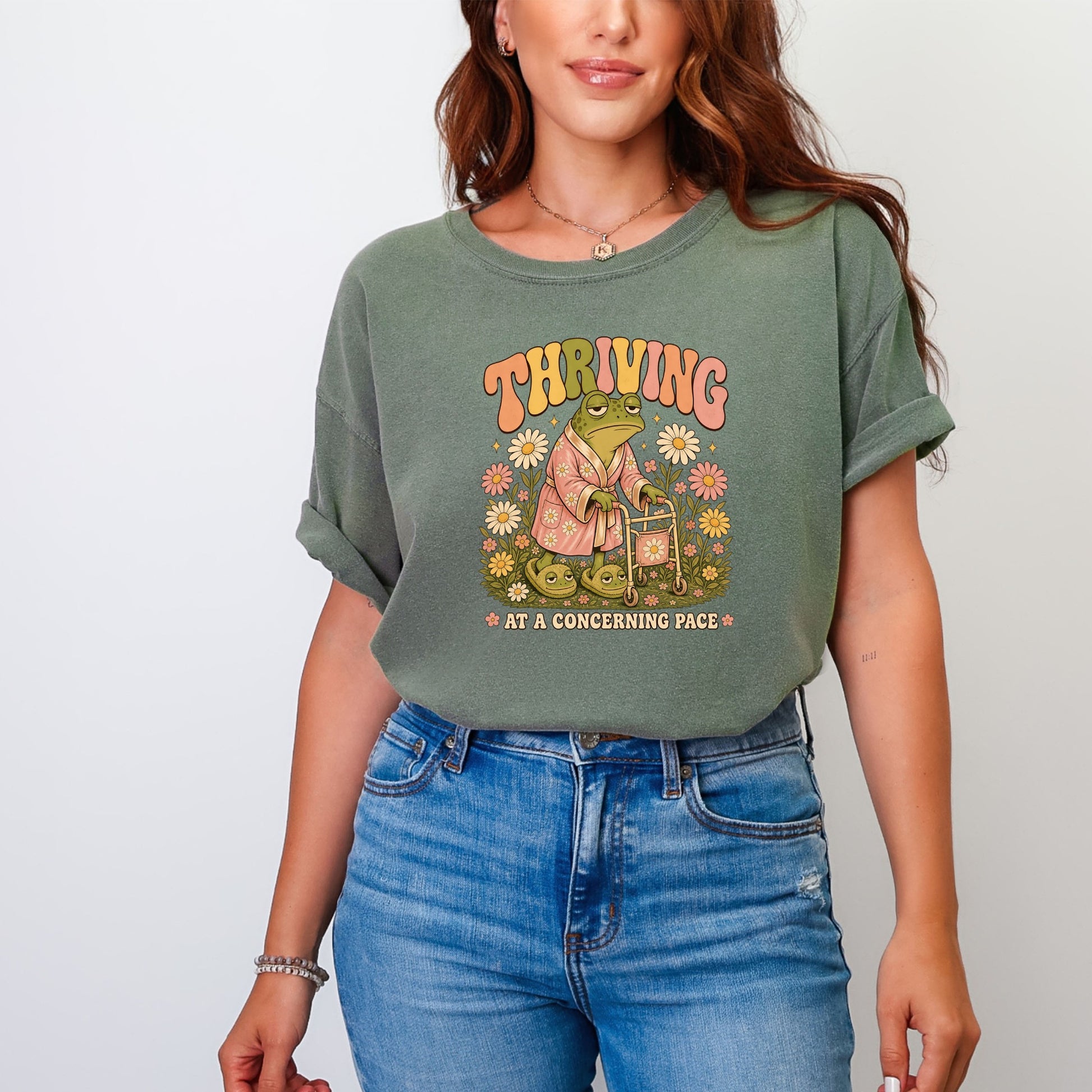 Retro graphic of a frog in a robe with a walker and flowers, text "THRVING AT A CONCERNING PACE".