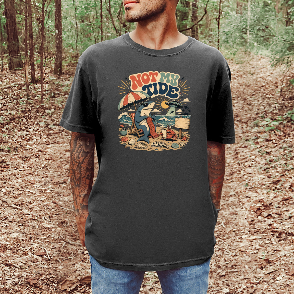 Graphic tee with text "NOT MY TIDE" featuring a shark knitting on a beach with a crab.