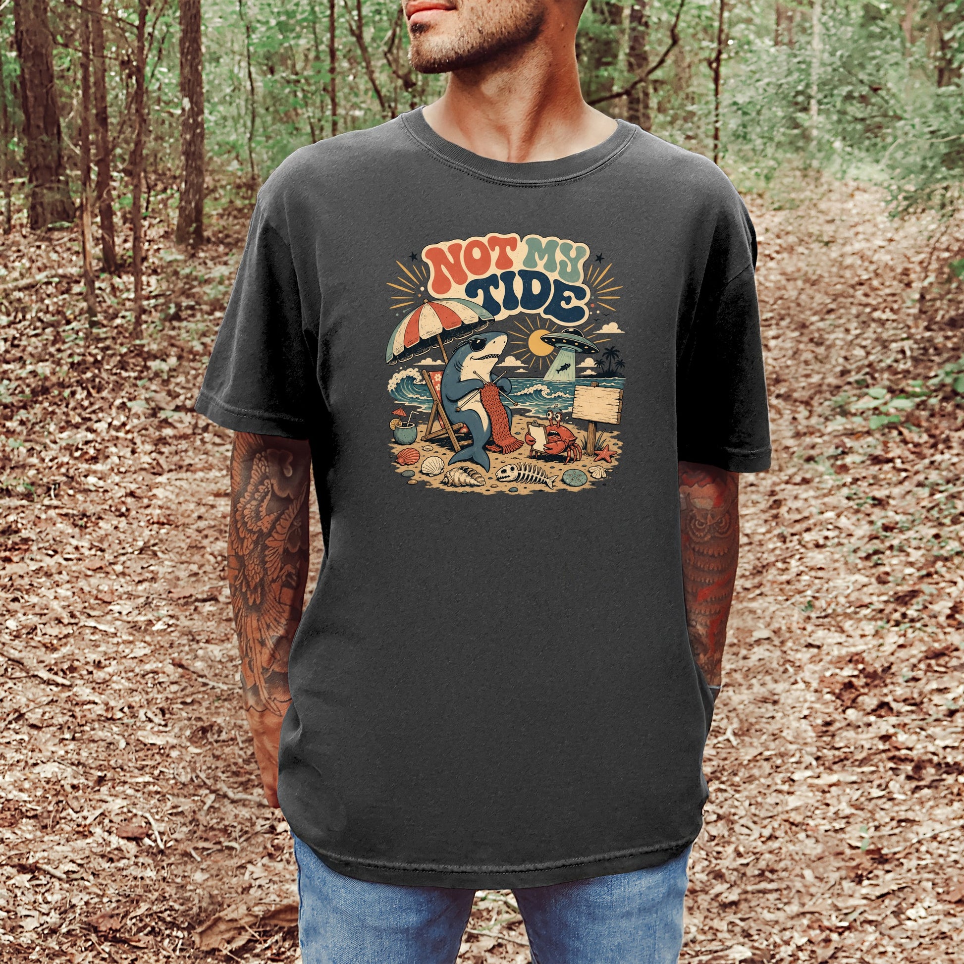 Graphic tee with text "NOT MY TIDE" featuring a shark knitting on a beach with a crab.