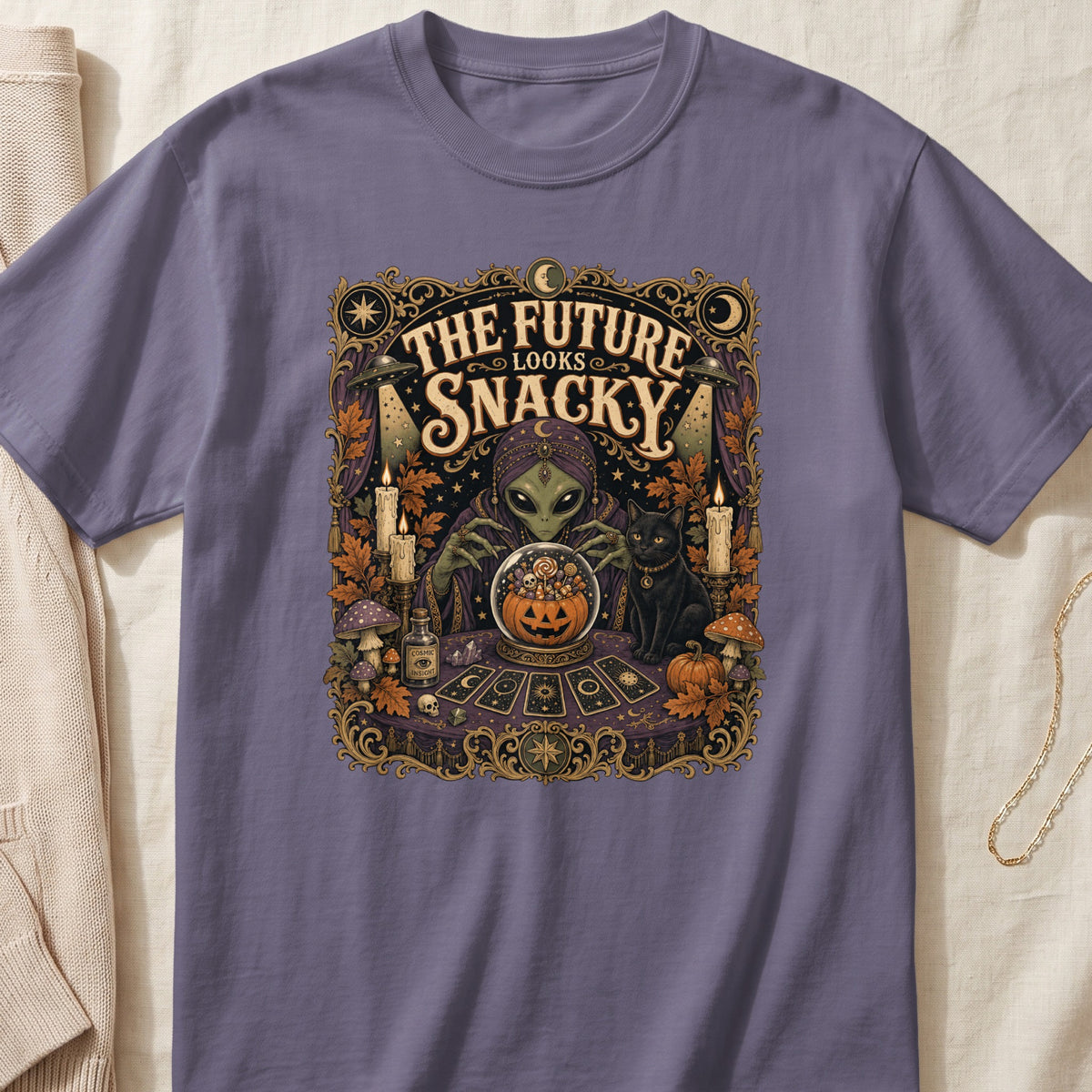 Alien fortune teller with crystal ball of candy, black cat, and tarot cards, text "The Future Looks Snacky".
