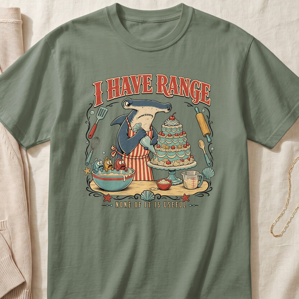 Hammerhead shark baking a cake with fish in a bowl; text says "I HAVE RANGE NONE OF IT IS USEFUL".